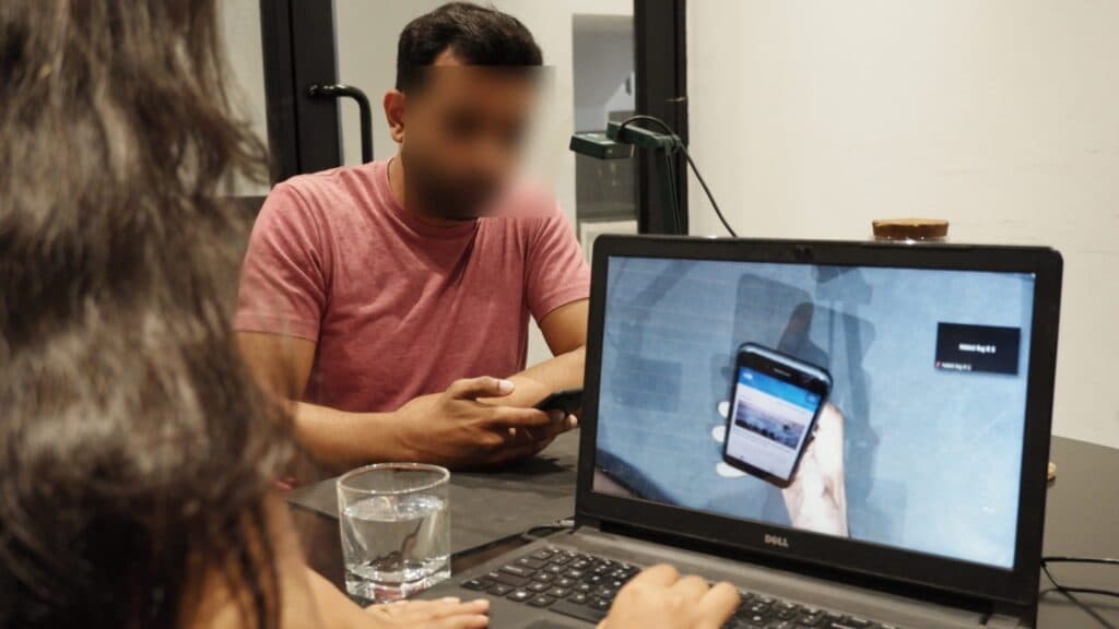 A participant using a phone while the moderator watches a live overhead view of their screen on a laptop